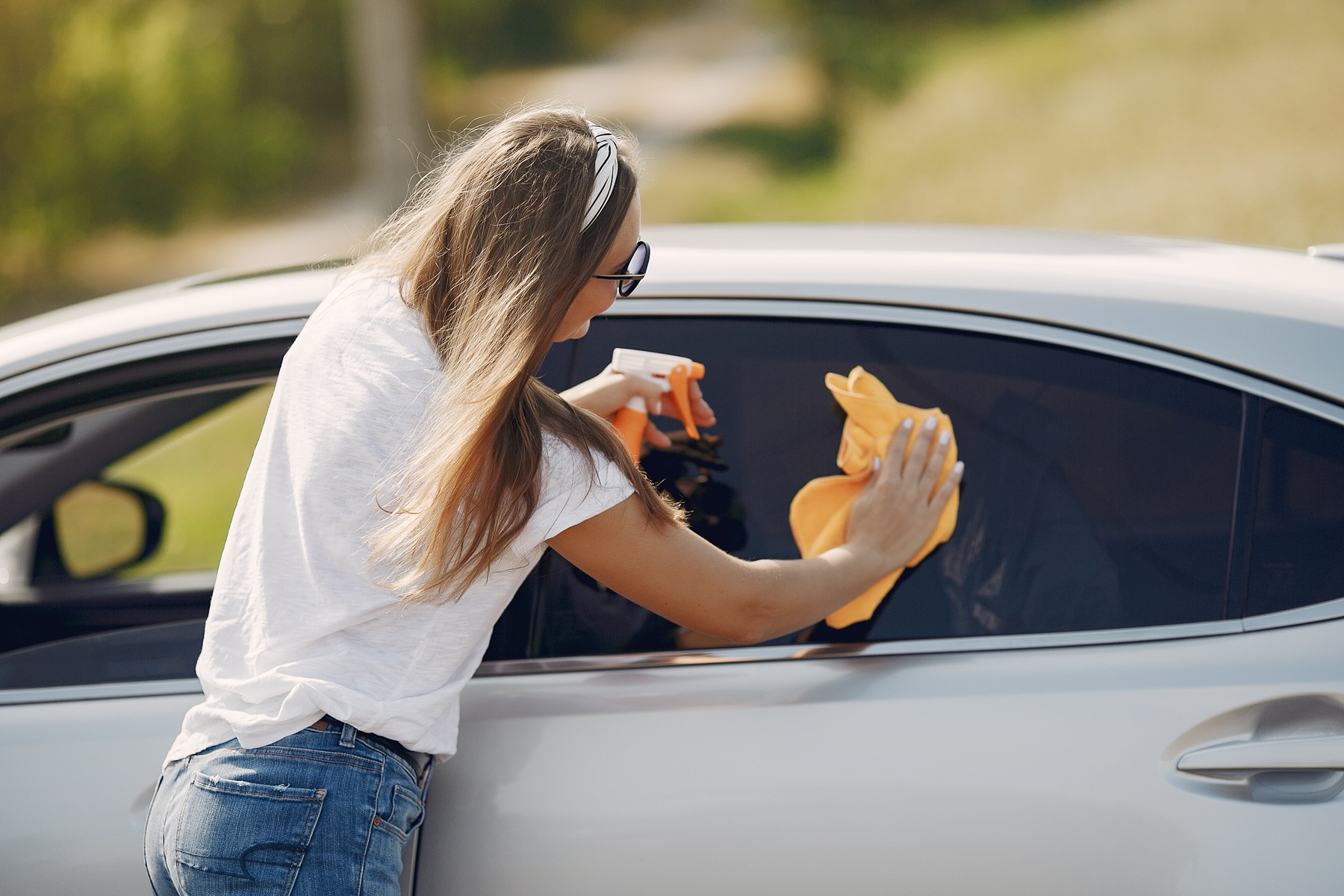 Woman by the car. Lady in a white t-shirt. Woman wipes the car
